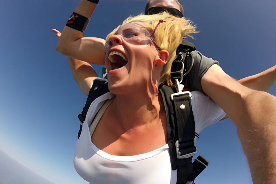 blonde-haired woman in white T-shirt loving her tandem skydive freefall experience