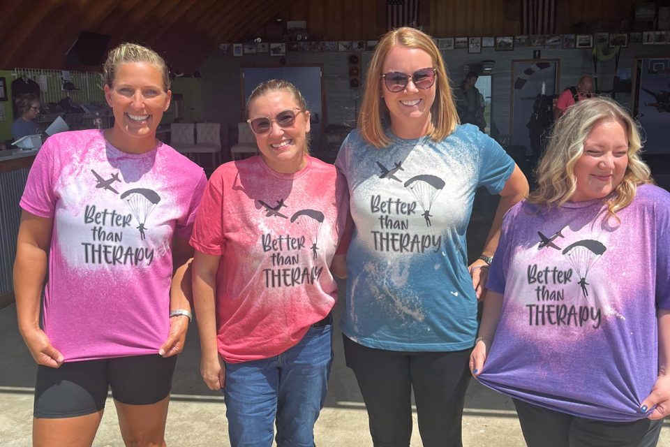 four women lined up wearing different colors of skydiving is better than therapy tshirts