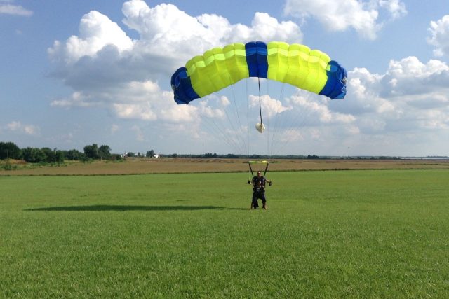 tandem skydiving student lands in the landing area under large blue and yellow canopy