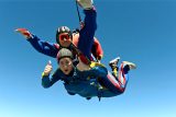 young woman gives thumbs up while tandem skydiving