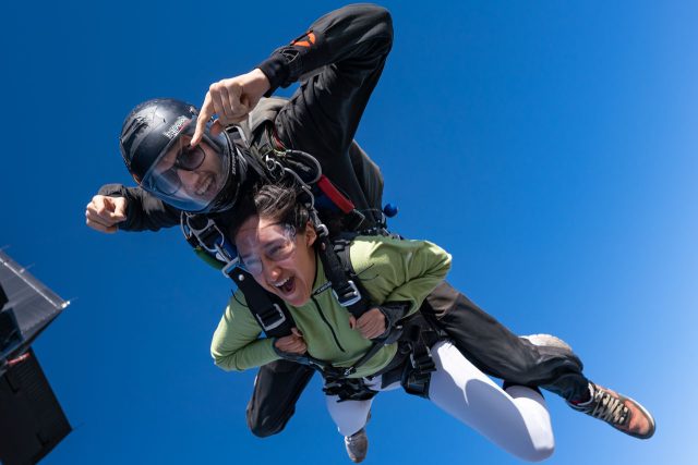 young woman in green jacket and white yoga pants smiles big after exiting the plane