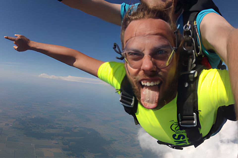 young man in bright yellow shirt sticks out his tongue while in skydiving freefall