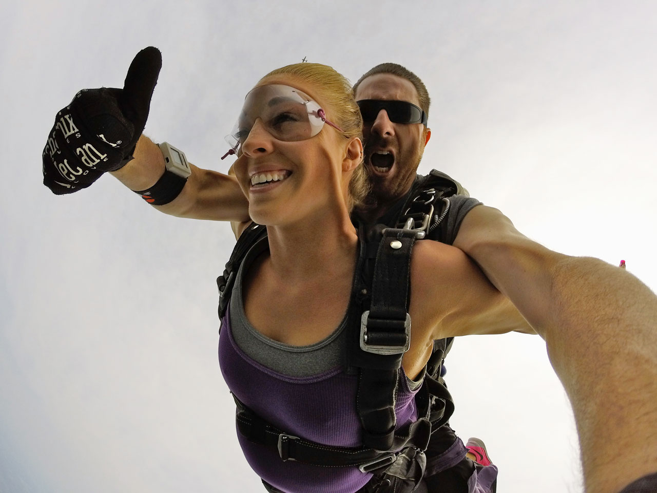 young woman in purple tank top smiles while freefalling during tandem skydive