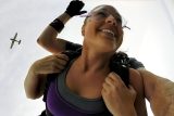 female tandem skydiving student in purple tank top smiles after exiting plane which is flying in the background