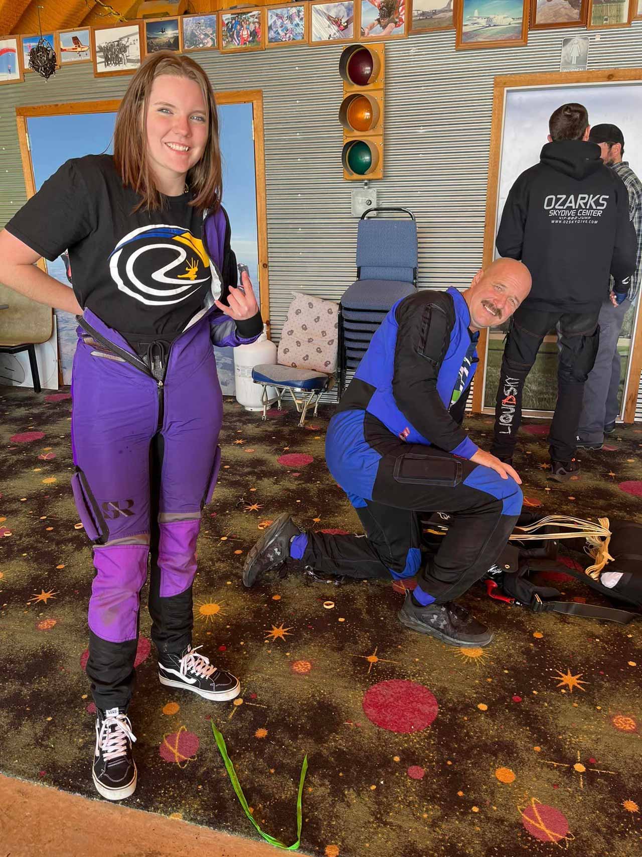 young woman in purple jumpsuit and OZARKS Skydive Center shirt gets ready to skydive