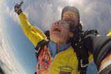 woman in yellow jumpsuit smiles in skydiving freefall