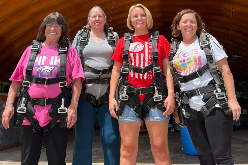 four women smile for a picture in front of the OZARKS Skydive Center hangar
