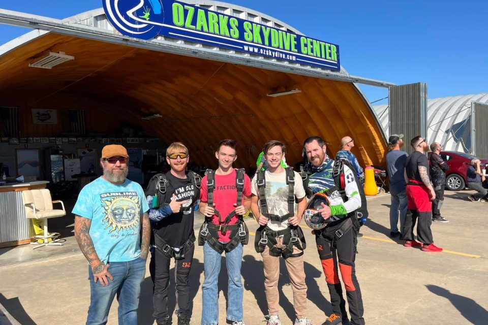 five guys of various ages pose for photo in front of Ozarks Skydive Center sign on hangar