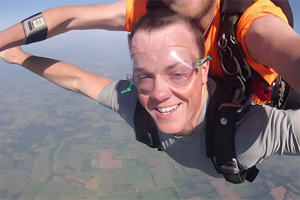 young man smiles with arms outstretched in skydiving freefall