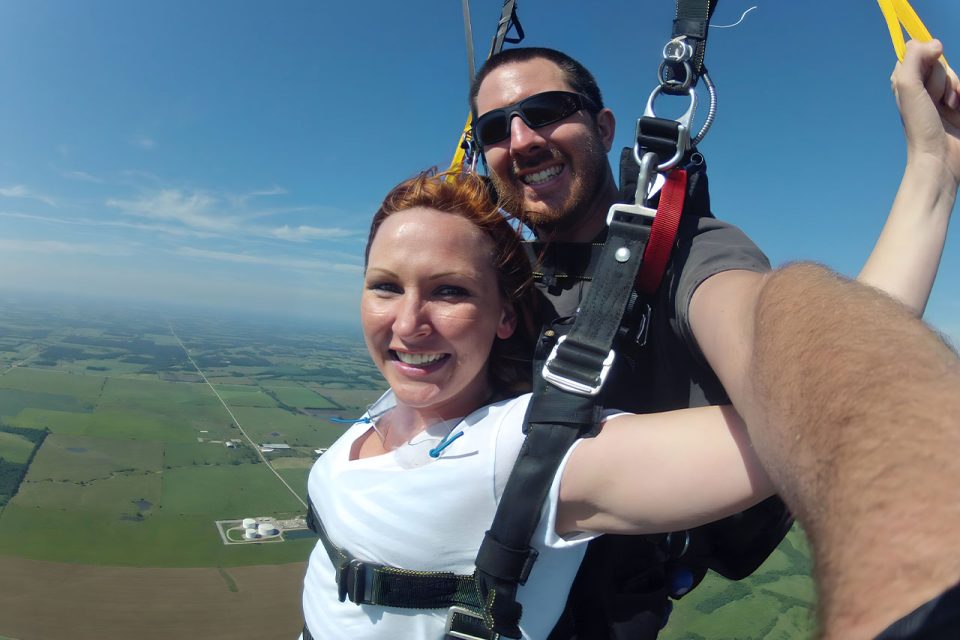 young woman in white shirt smiles under canopy with tandem instructor