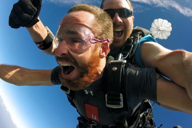 red-haired man smiles big while in skydiving freefall