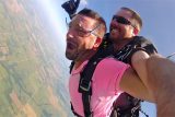 man in hot pink shirt has mouth open in excitement while in skydiving freefall