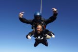young woman with black addidas sweathshirt and white gloves gives two thumbs up while in freefall
