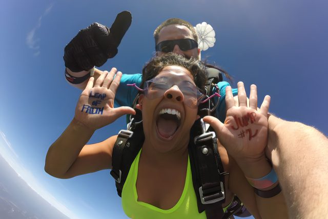 woman in yellow tank top smiles while in freefall with leap of faith jump #2 written on her hands