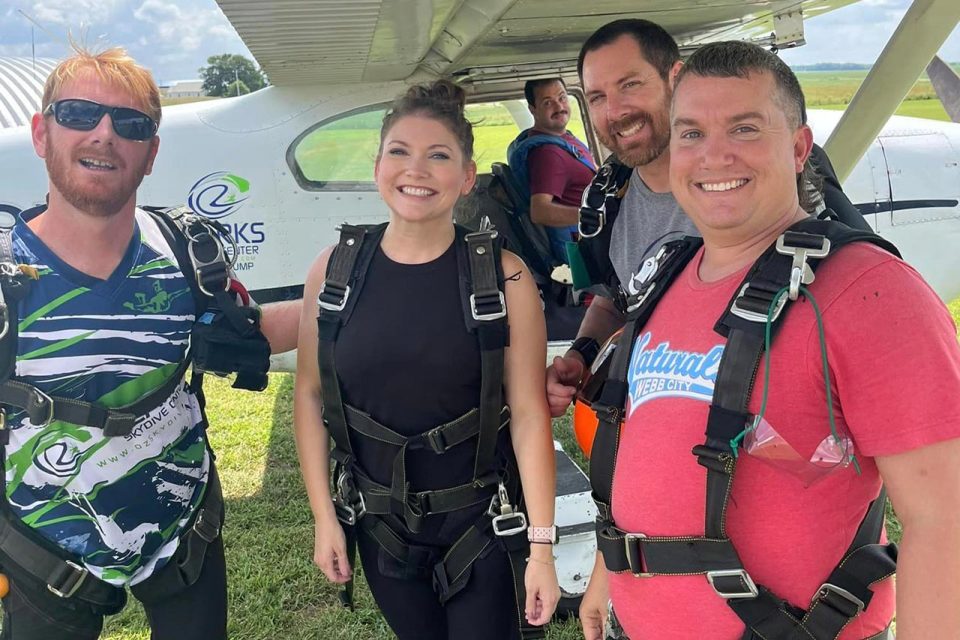 group of tandem skydivers smiles for the camera before boarding the skydiving aircraft